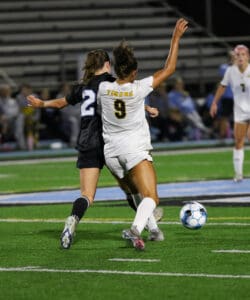 Soccer players competing for the ball during a match on a grassy field at night.
