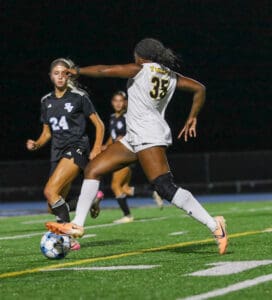 Two soccer players in action on a field at night, competing for possession of the ball.