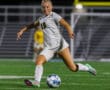 Soccer player in white uniform kicking ball on field at night under stadium lights.