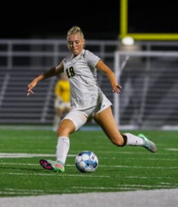 Soccer player in white uniform kicking ball on field at night under stadium lights.