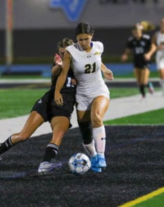 Two soccer players compete for the ball during a night match on a field with vibrant colors.