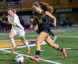 Two female soccer players competing during a nighttime soccer match on a field.