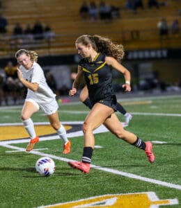 Two female soccer players competing during a nighttime soccer match on a field.