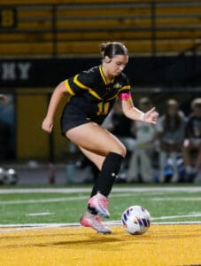 Soccer player in action during a night match, dribbling the ball on the field with focused determination.