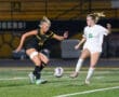 Two female soccer players compete for the ball on a field during a night game.