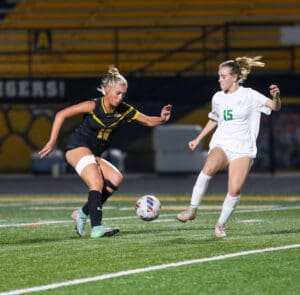 Two female soccer players compete for the ball on a field during a night game.