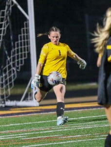 Soccer goalie in yellow jersey kicking ball during night match, focused on gameplay.