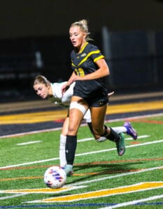 Soccer player in black uniform dribbles ball on field during night game.