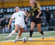 Two female soccer players competing for the ball on a field during a game.