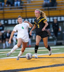 Two female soccer players competing for the ball on a field during a game.
