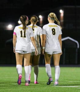 Soccer players in white uniforms walking on a field at night, back view.