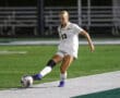 Soccer player in white jersey kicking ball during a match on field. Sports action shot.