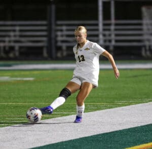 Soccer player in white jersey kicking ball during a match on field. Sports action shot.