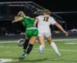 Two female soccer players in motion during a night game, competing for the ball on the field.
