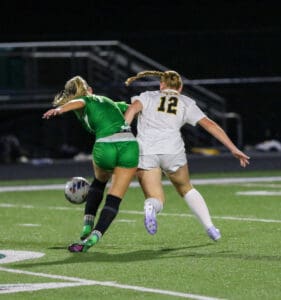 Two female soccer players in motion during a night game, competing for the ball on the field.