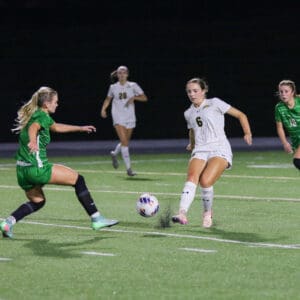 Soccer players in action during a night match, player in white passes the ball to teammate on field.