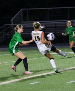 Two soccer players in action on the field at night, one in green and one in a white Tigers jersey.