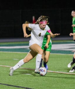 Soccer player in white jersey dribbles past defender during nighttime match on grass field.