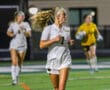 Female soccer player in white uniform runs on field during night game.