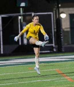 Goalkeeper in yellow jersey kicking the ball during a night soccer match.