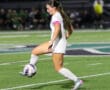 Soccer player in white uniform dribbles ball during night game on grass field.