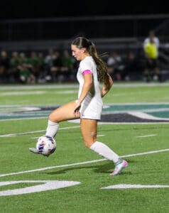 Soccer player in white uniform dribbles ball during night game on grass field.