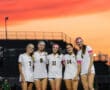 Teen soccer team posing on field at sunset, wearing white uniforms, smiling energetically.