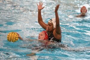 Water polo players in action, one holding the ball, another defending, splashing water in a competitive game.