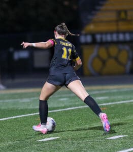 Soccer player in black jersey dribbles ball on field during night match, showcasing athletic skill and determination.