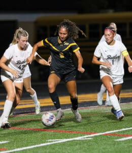 Soccer players in action during a competitive match at night on a grass field.