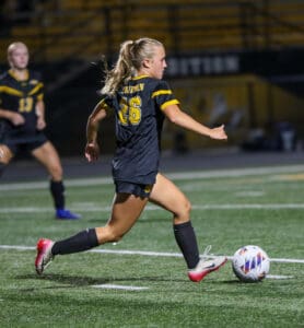 Soccer player in black and yellow uniform dribbling the ball on a field during a night game.