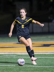 Soccer player in black jersey focuses on controlling the ball during a match on a green field.