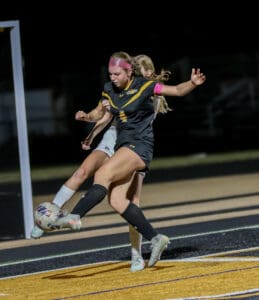 Soccer player in action, kicking ball during night match on turf field.