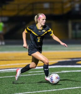 Soccer player in black jersey with number 7 dribbles on field during night game.
