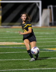 Soccer player in black kit controls the ball on a field during a night match.