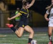 Soccer player in black uniform kicking ball during a night match on a field.