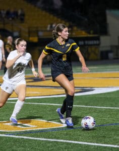 Two female soccer players in action on the field at night, focusing on the ball.