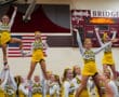 Cheerleaders in yellow Tigers uniforms performing energetic stunts in a gym with an American flag backdrop.