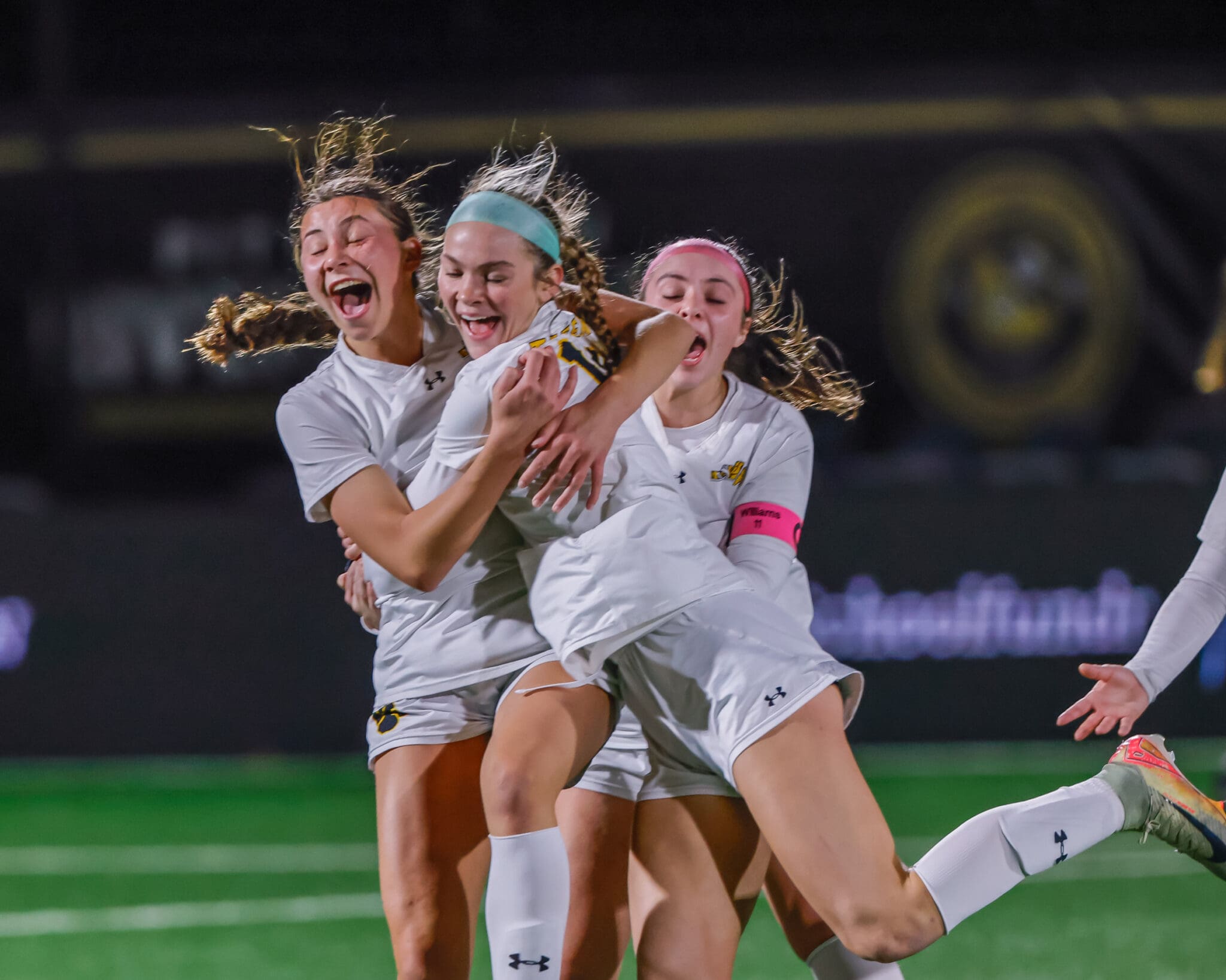 Soccer players celebrate a victory on the field, showing excitement and teamwork, under the stadium lights.