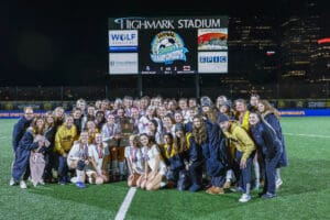 Girls' soccer team celebrates championship victory at Highmark Stadium under night lights.