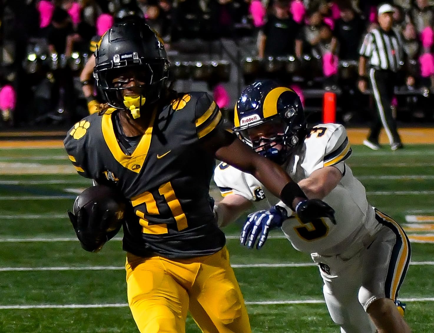 Football player in black and yellow jersey evades a tackle during a night game on the field.