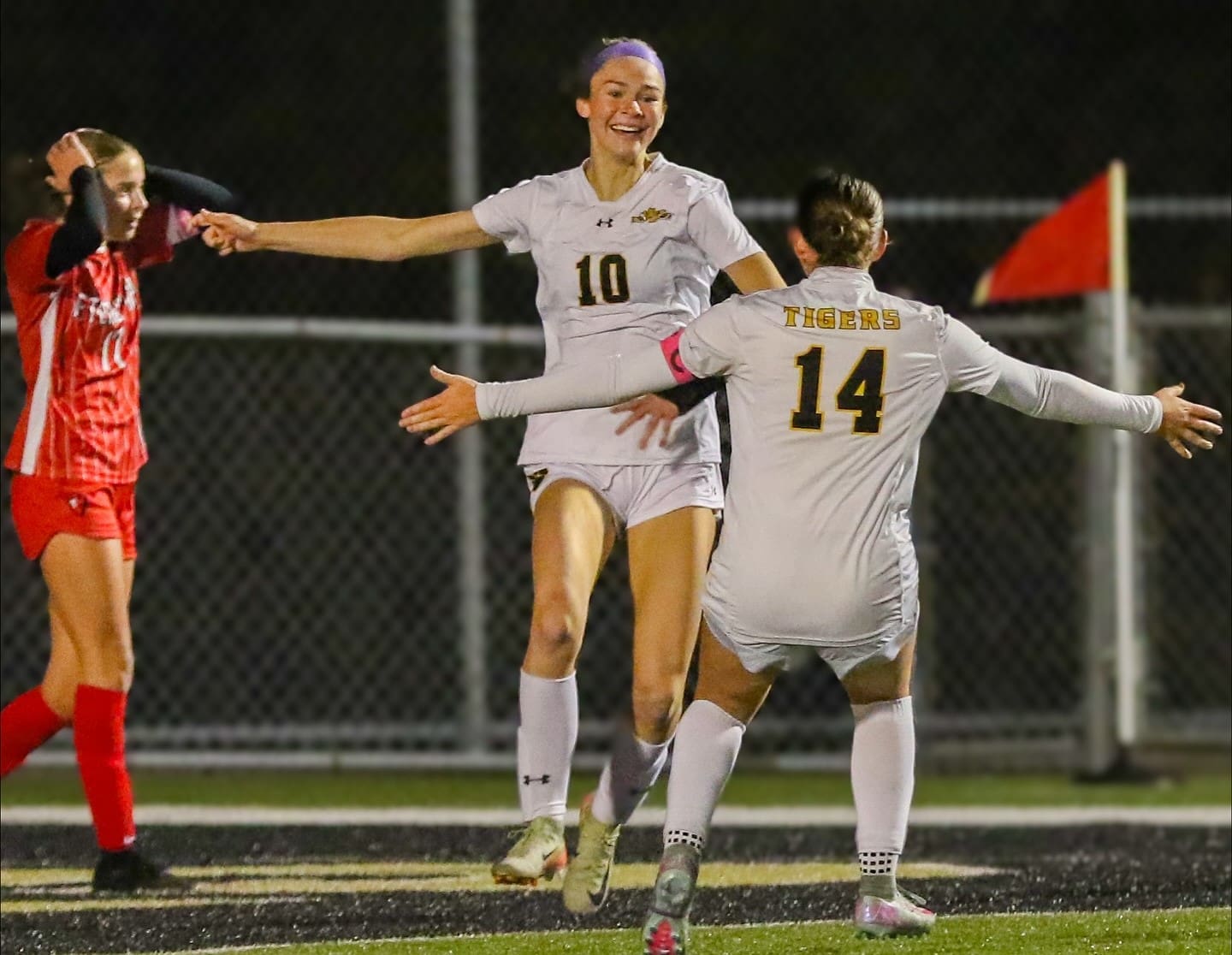 Soccer player jumps in celebration wearing number 10 jersey, greeted by teammate in a night match.
