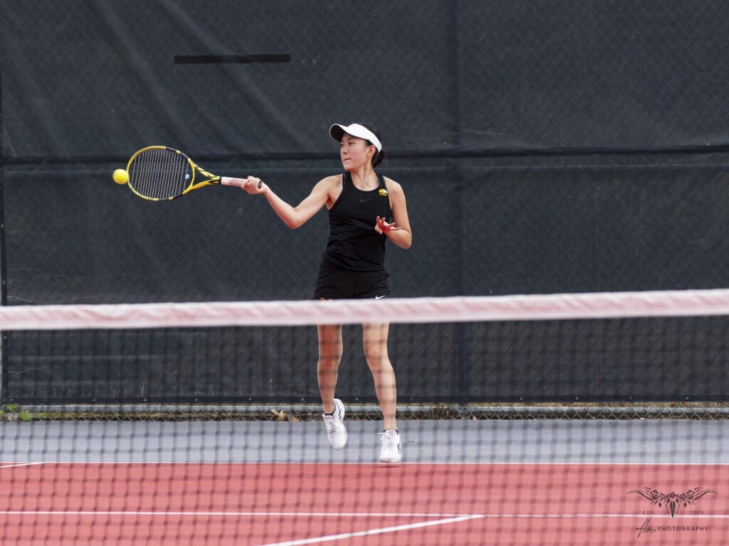 Tennis player hitting a forehand on a court, wearing black outfit and visor.
