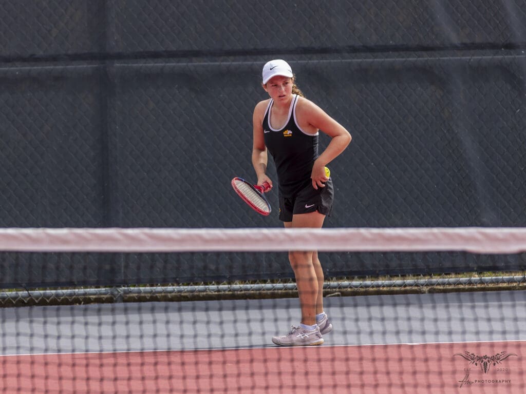 Young female tennis player ready to serve on court, holding racket and ball.