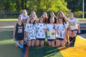 High school field hockey team posing on the field in custom shirts, celebrating teamwork and sportsmanship.