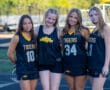 Four girls in Tigers sports uniforms smiling on a track field.