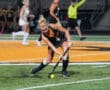 Field hockey player in action during a game at night on a green and orange field.