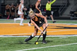 Field hockey player in action during a game at night on a green and orange field.