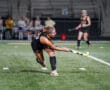 Field hockey player striking the ball on a lit field during a match.