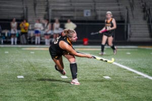 Field hockey player striking the ball on a lit field during a match.
